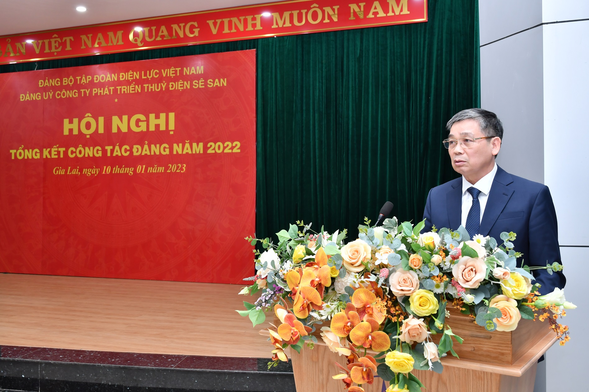 A person standing at a podium with flowers in front of himDescription automatically generated with medium confidence